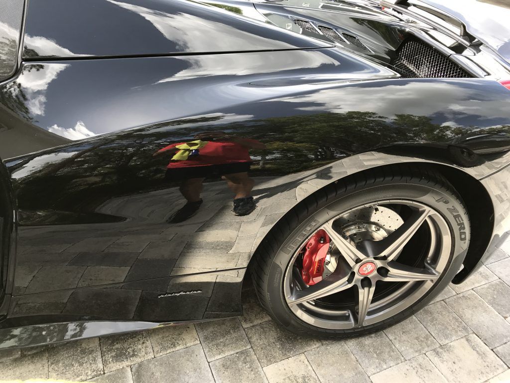 A black sports car with red brake calipers is parked on a brick driveway.
