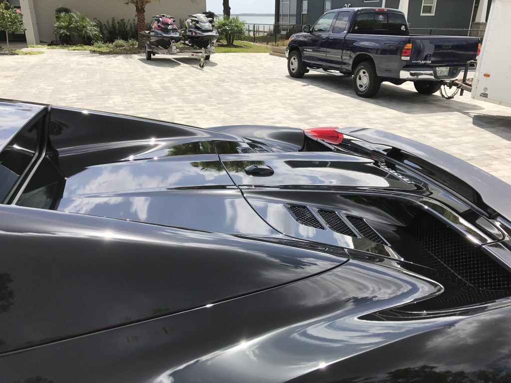 A black car is parked in a driveway next to a blue truck.