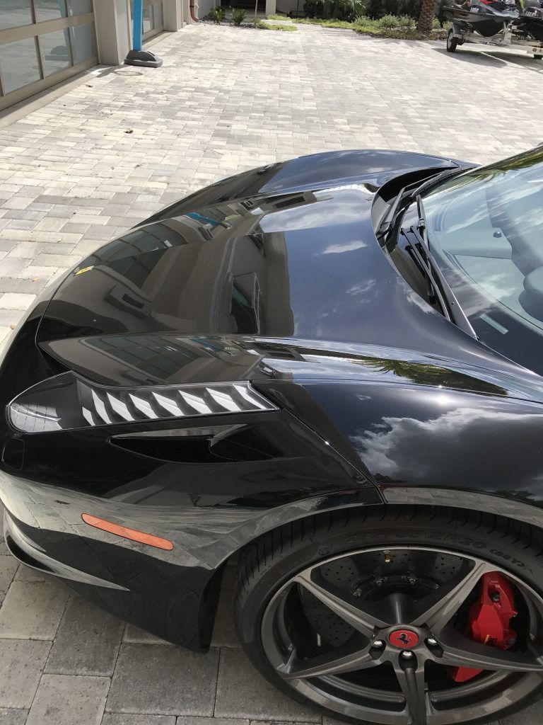 A black sports car is parked on a brick driveway.