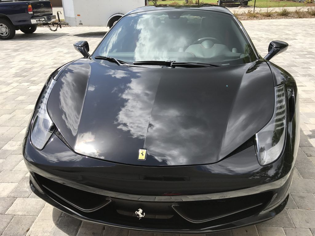 A black ferrari sports car is parked on a brick driveway.