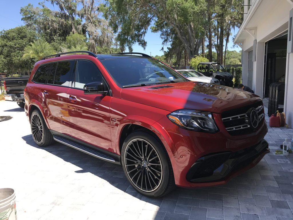A red mercedes benz gls 63 amg is parked in front of a garage.