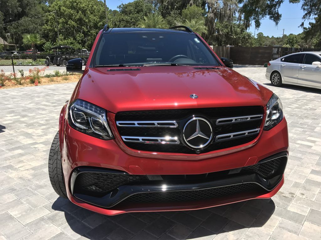 A red mercedes benz is parked in a parking lot.