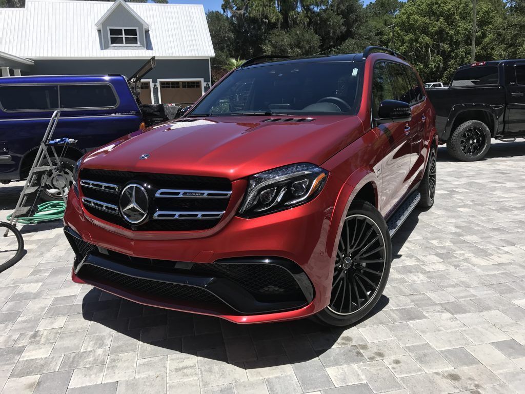 A red mercedes benz gls 63 amg is parked in front of a house.