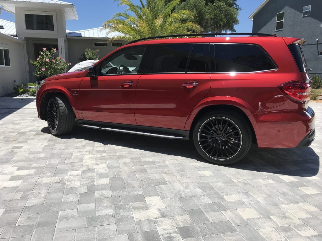A red suv is parked on a brick driveway in front of a house.
