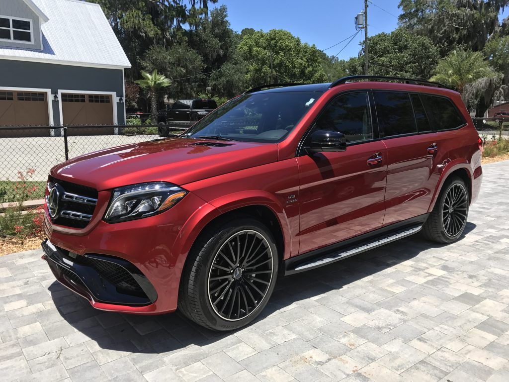 A red mercedes benz gls 63 amg is parked in front of a garage.