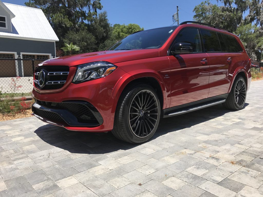 A red mercedes benz gl63 amg is parked on a brick driveway.