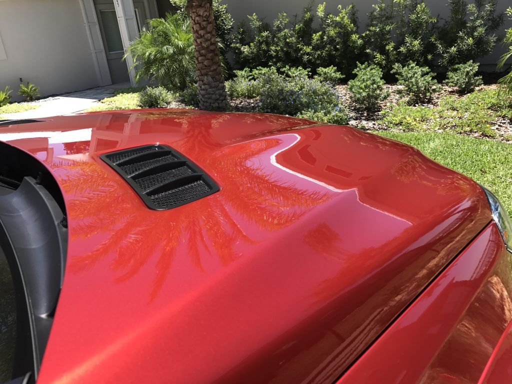 A close up of a red car hood with a hood scoop.