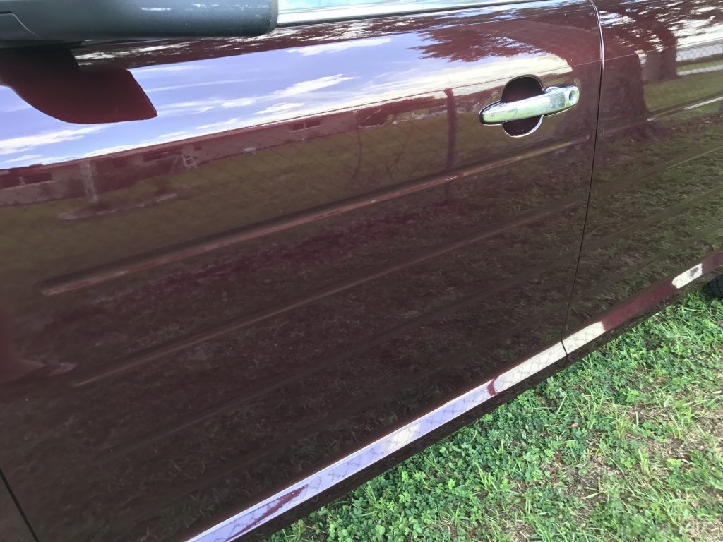 A burgundy car is parked in the grass with the door open