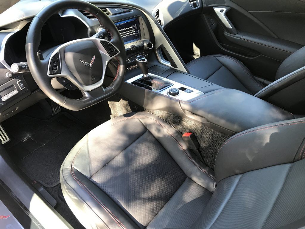 The interior of a white corvette with black leather seats and a steering wheel.