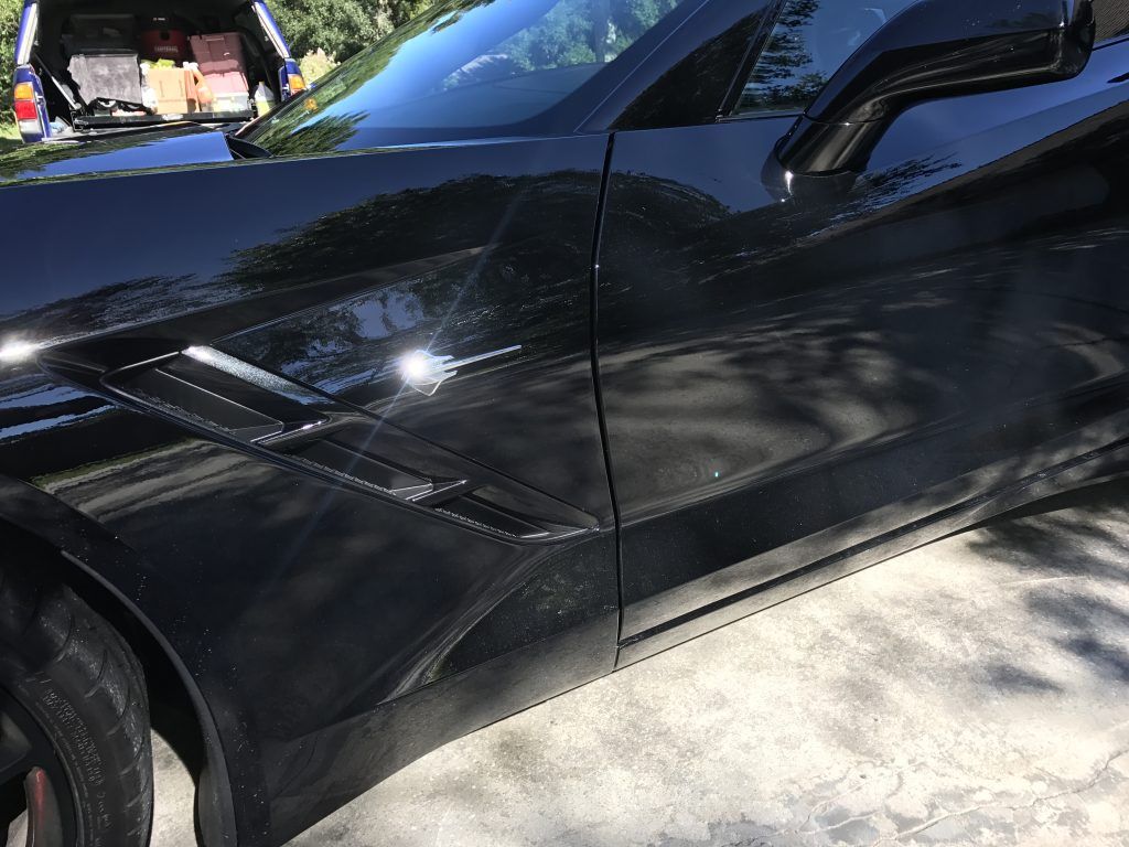 A black car is parked in a driveway with the trunk open.