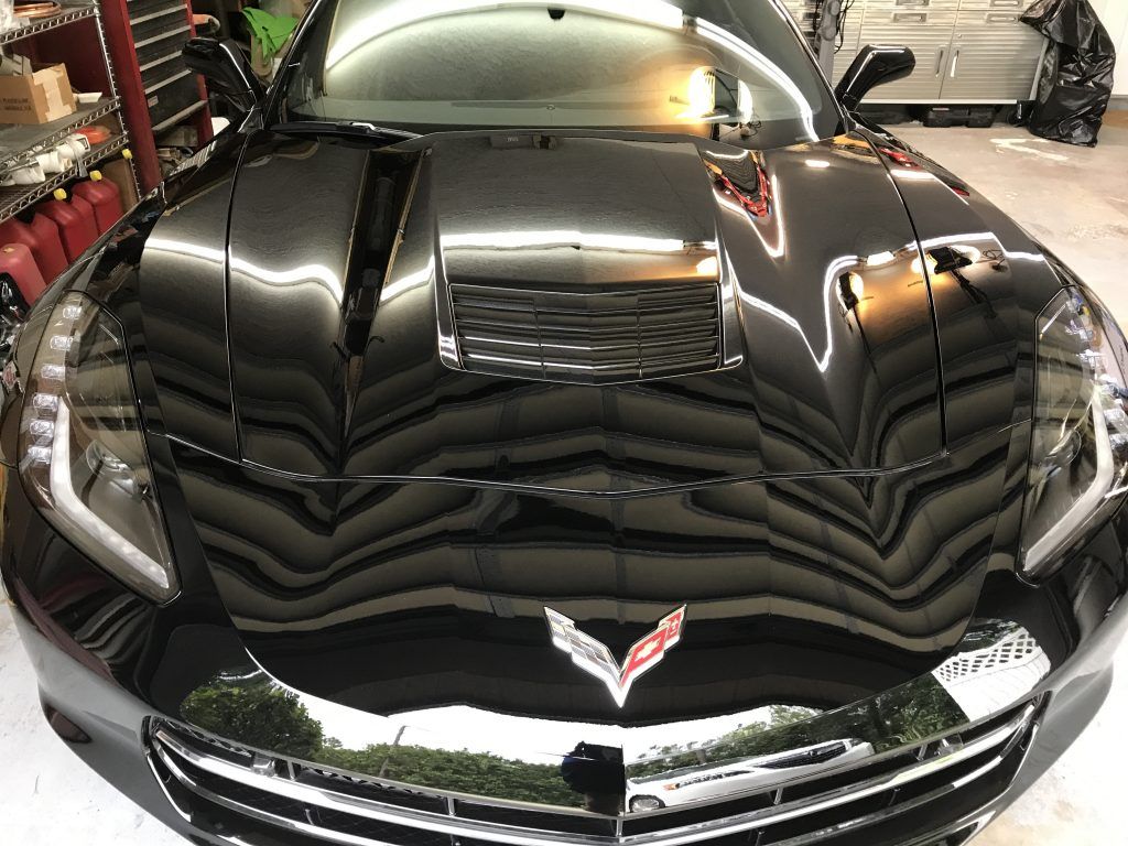 A black corvette is parked in a garage with the hood up.