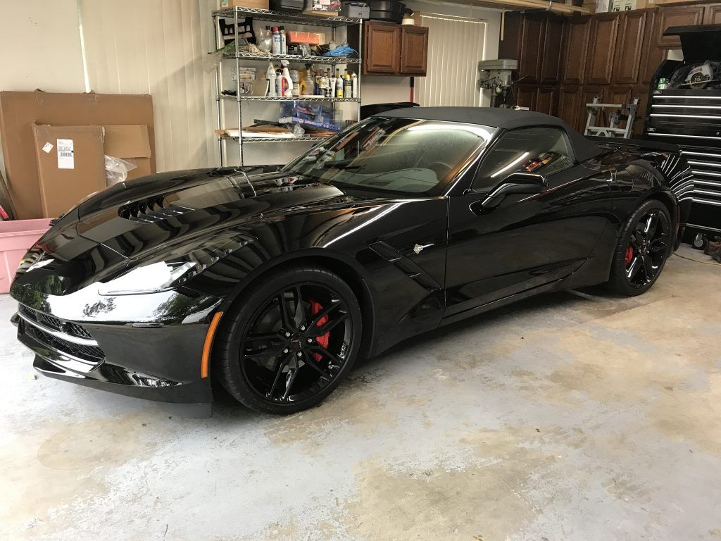 A black corvette convertible is parked in a garage.