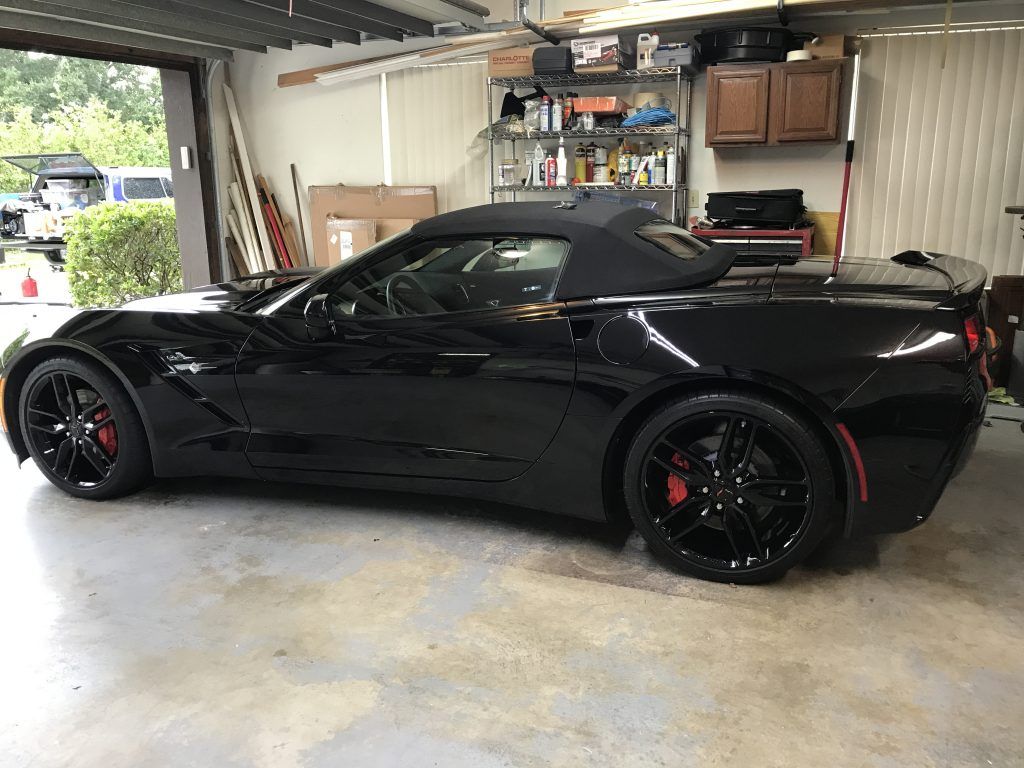 A black corvette convertible is parked in a garage.