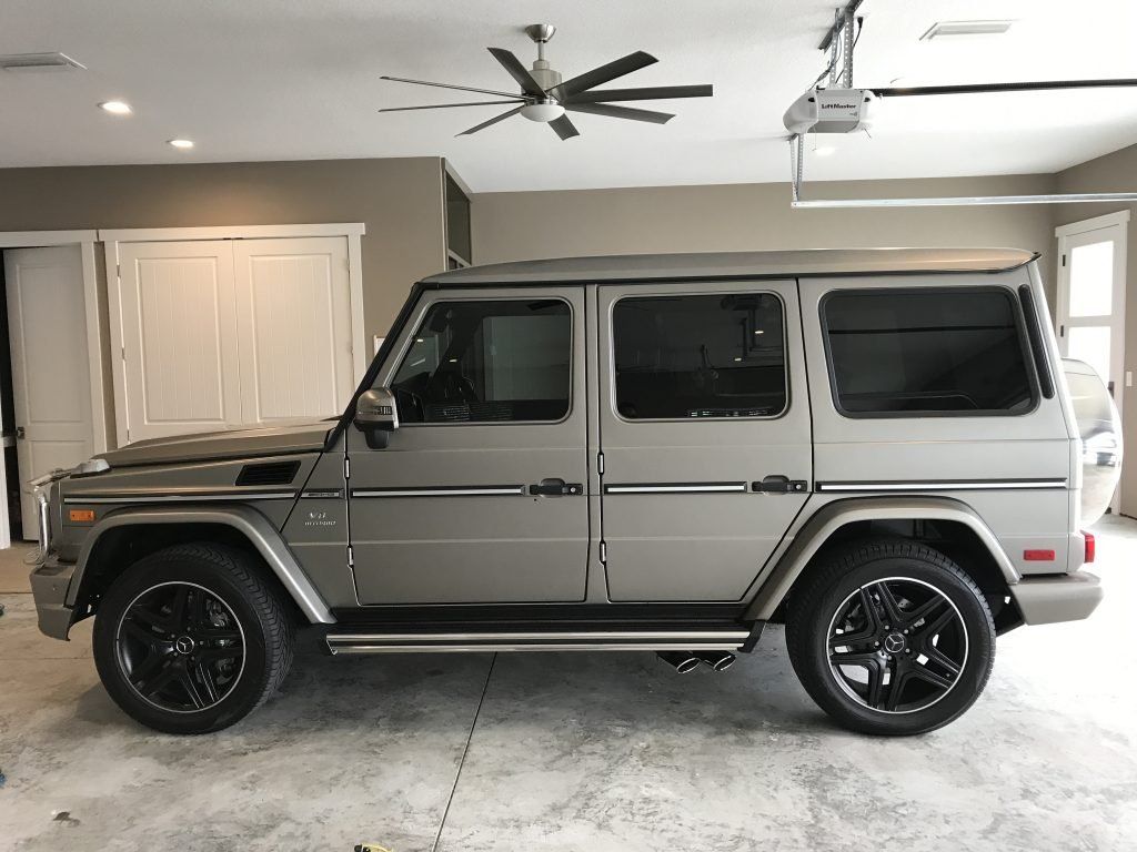 A silver mercedes benz g63 is parked in a garage with a ceiling fan.