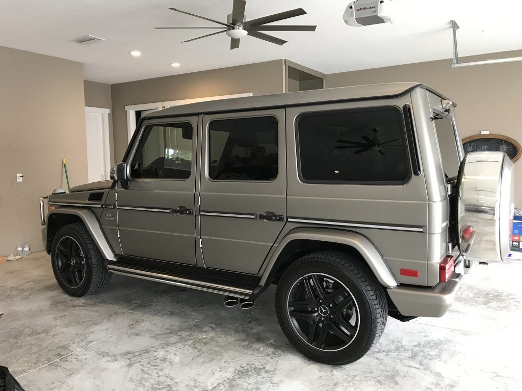 A mercedes benz g63 is parked in a garage with a ceiling fan.
