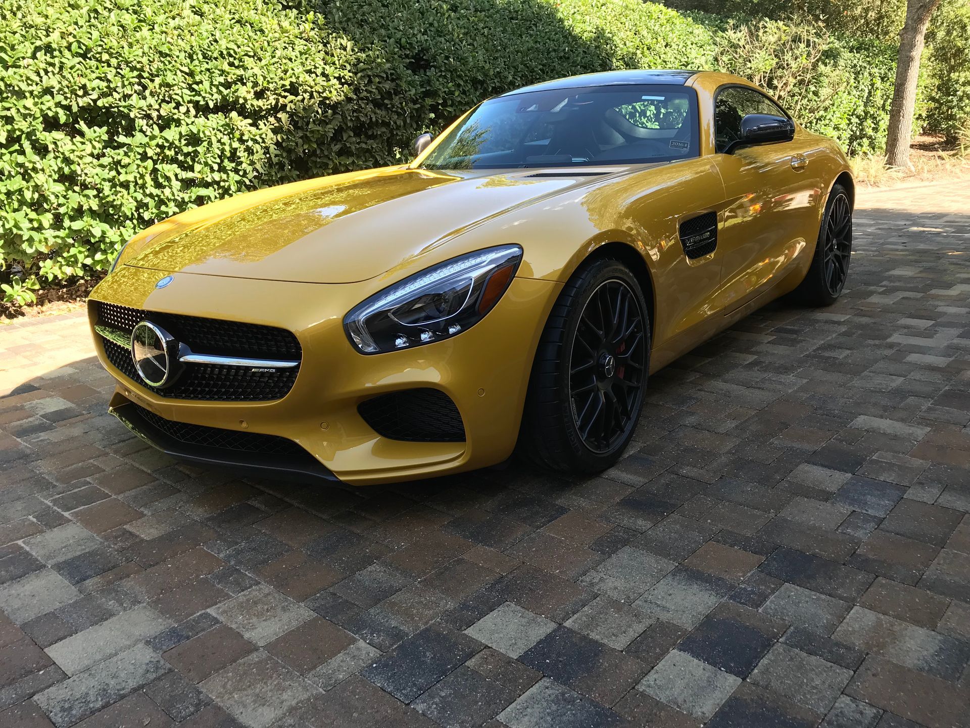 A yellow mercedes benz amg gt is parked on a brick driveway.