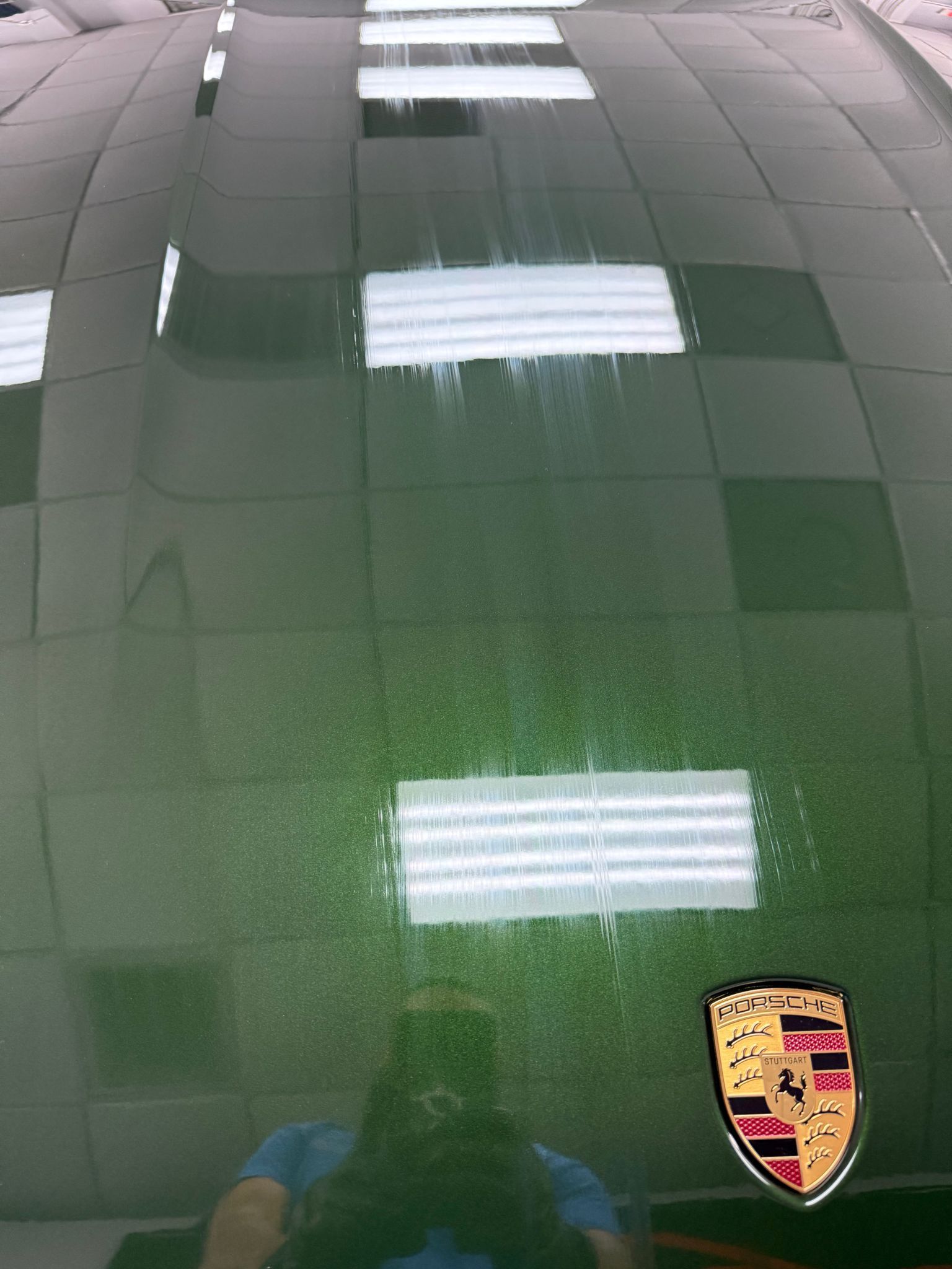 Green Porsche hood with white light reflections, and the Porsche emblem.