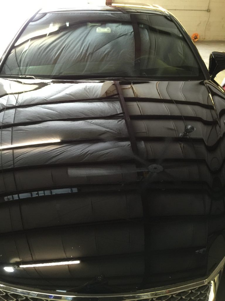 A black car is parked in a garage with the hood up.