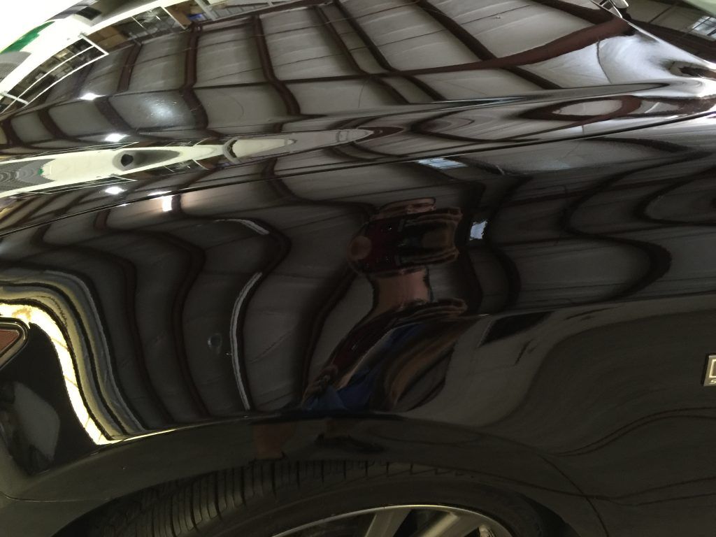 A black car is parked in a garage with a reflection of a building in the hood.