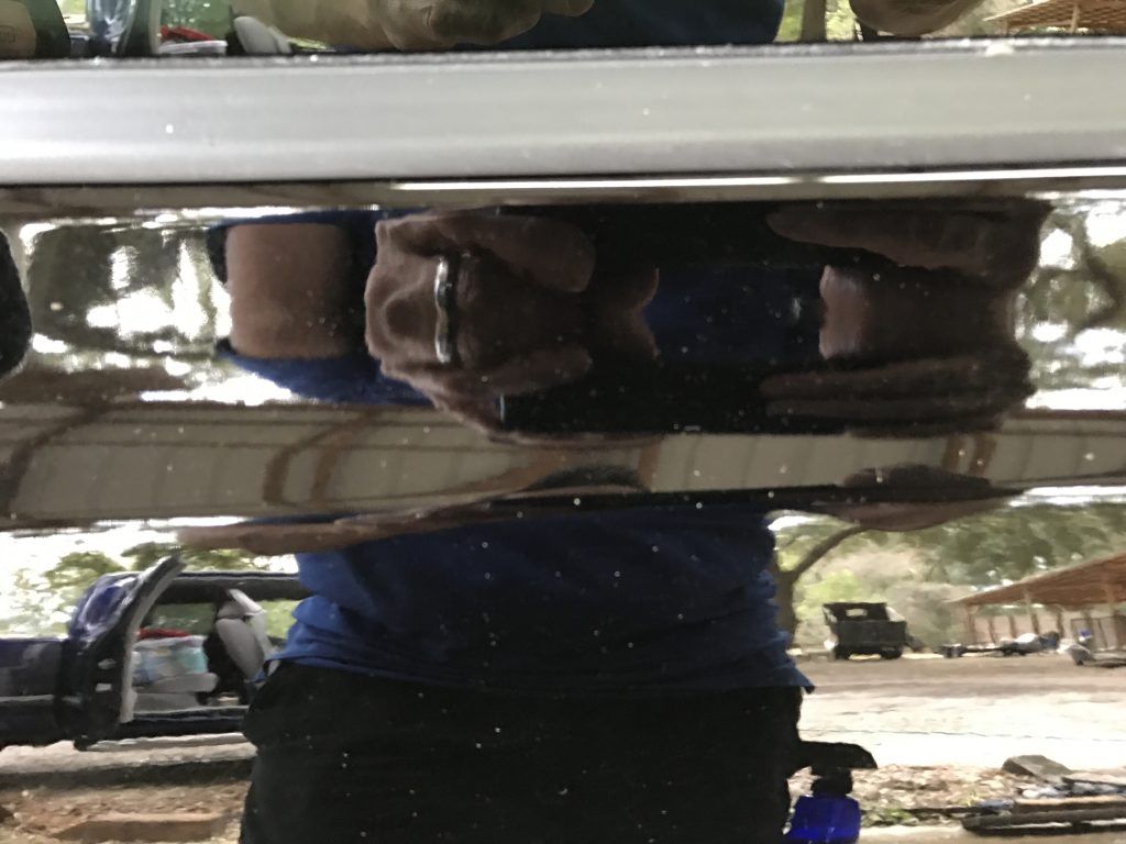 A person is standing under a car with their reflection in the mirror