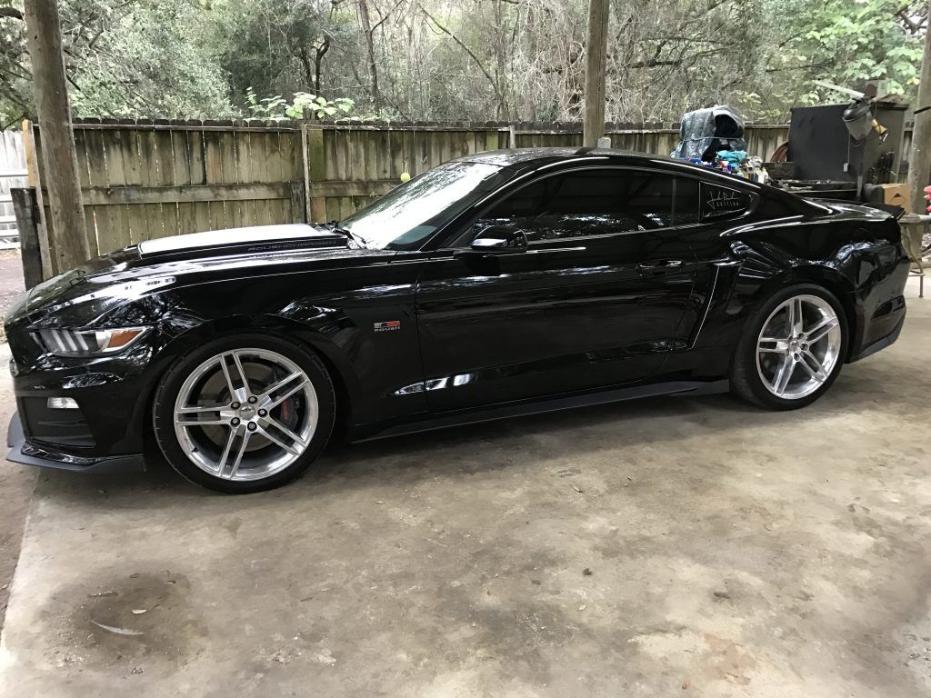 A black mustang is parked in a driveway next to a fence.