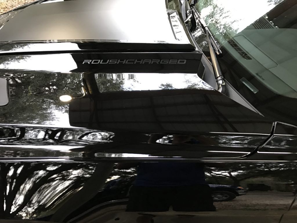 A black car is parked in a parking lot with the hood up.