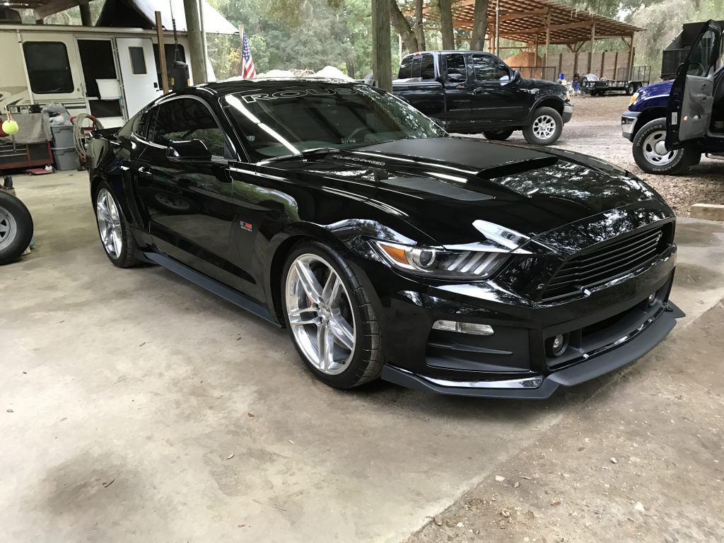 A black mustang is parked in a garage next to a truck.