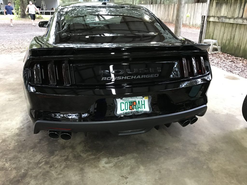 A black mustang with a license plate that says cobrah is parked in a driveway.