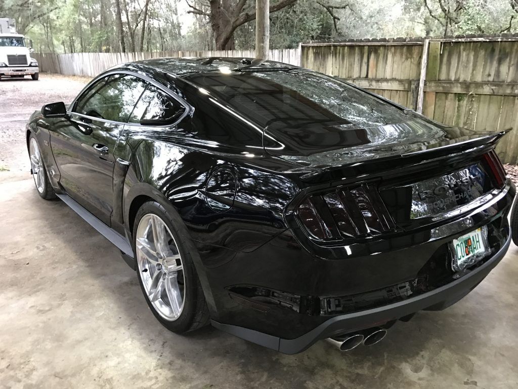 A black ford mustang is parked in a driveway next to a fence.