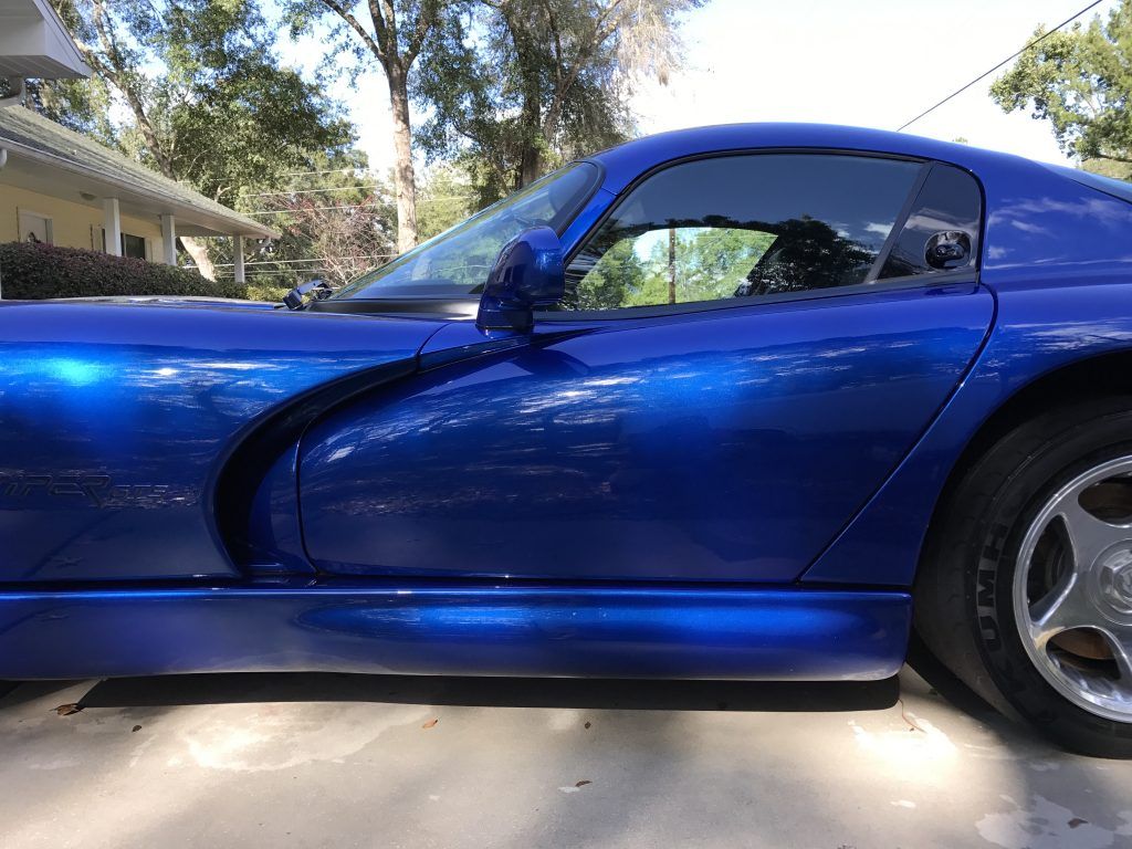 A blue dodge viper is parked in a driveway in front of a house.
