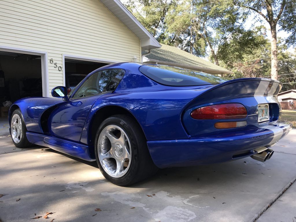 A blue dodge viper is parked in front of a garage.