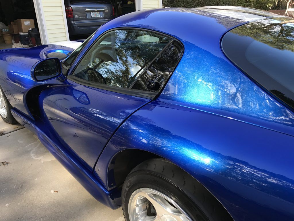 A blue sports car is parked in a driveway in front of a garage.