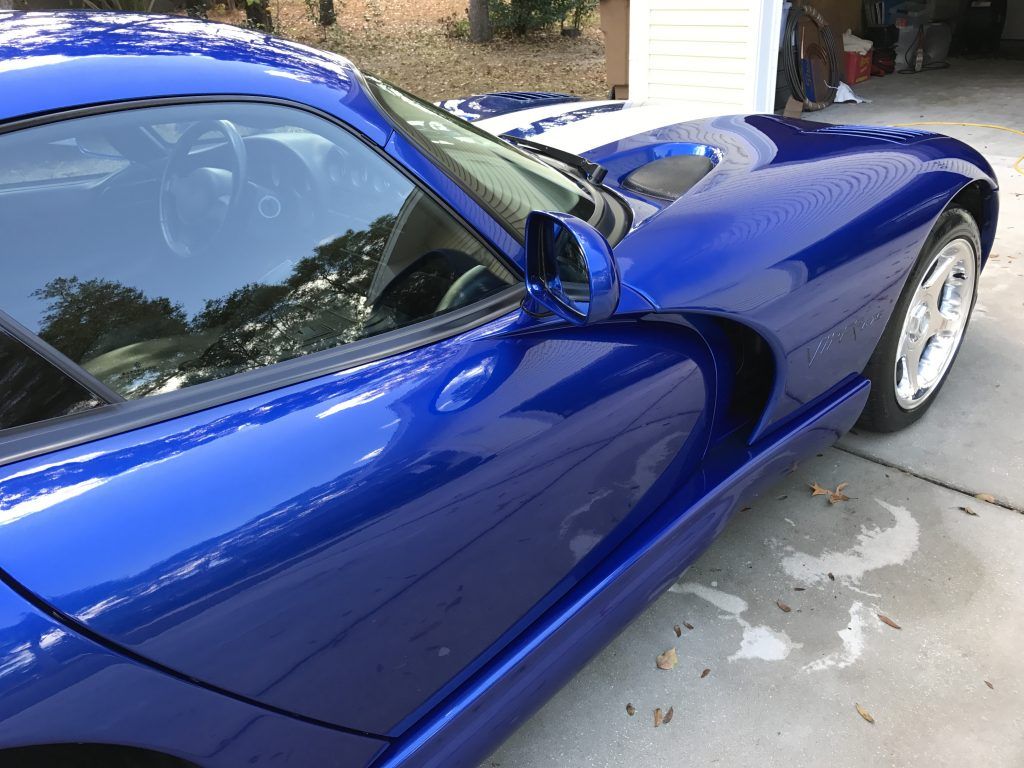 A blue sports car is parked in a driveway next to a garage.