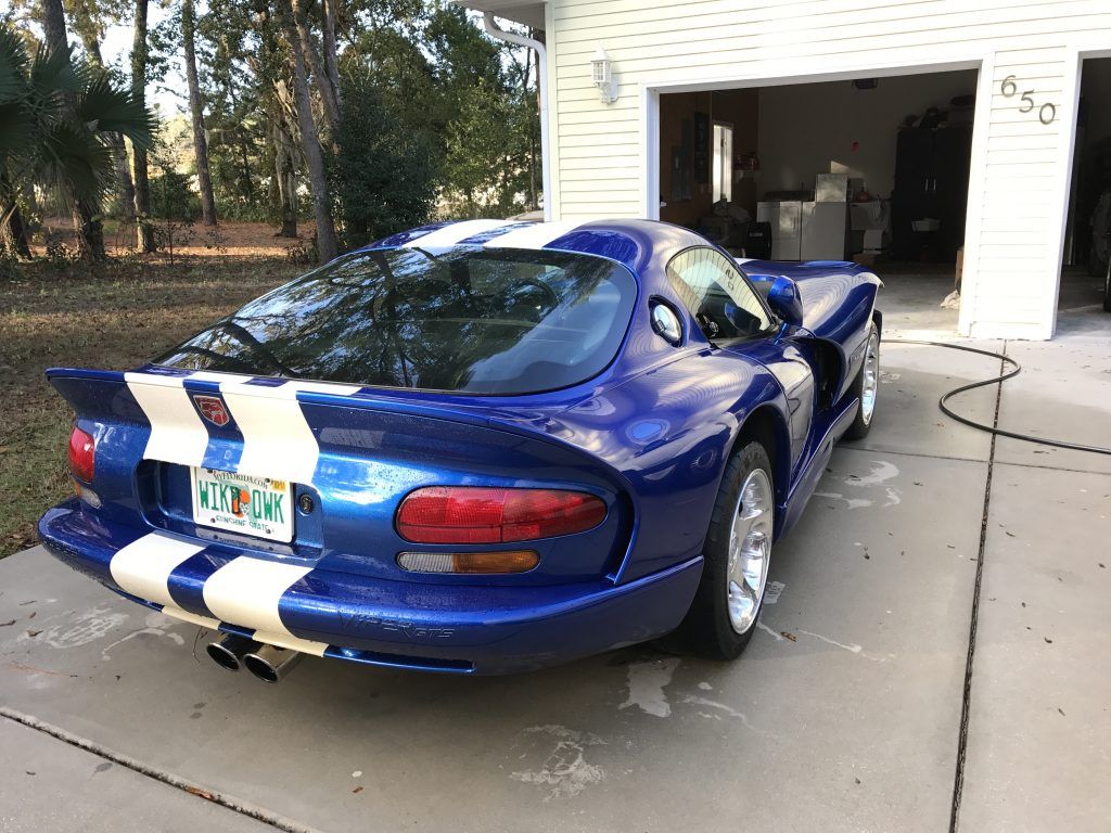 A blue and white sports car is parked in front of a garage.