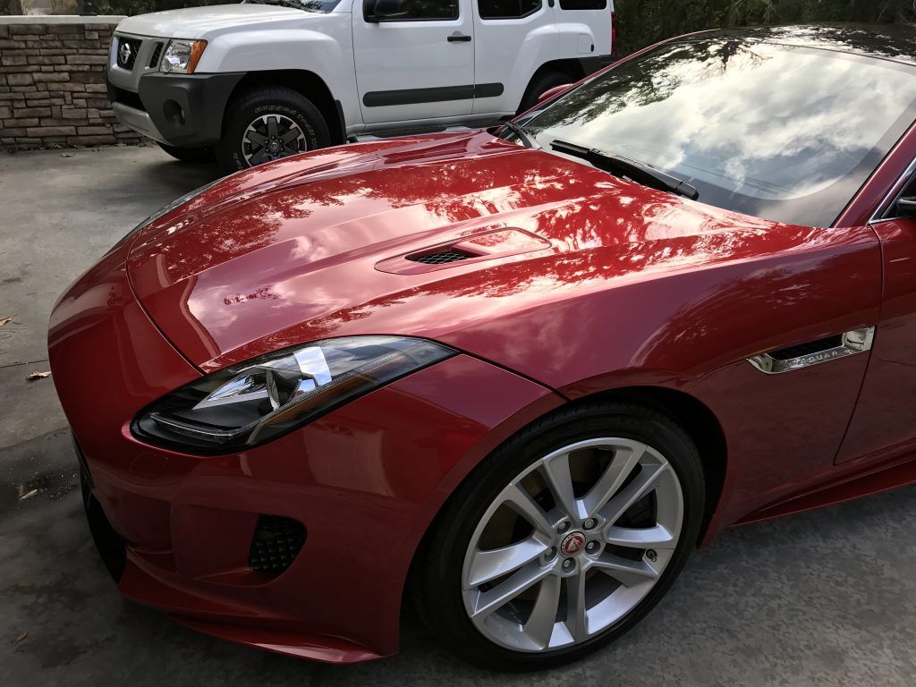 A red sports car is parked in a driveway next to a white suv.