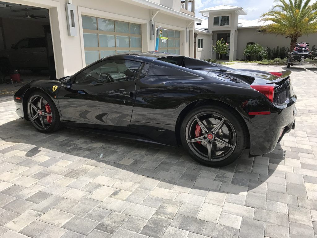 A black ferrari 458 spider is parked in front of a garage.