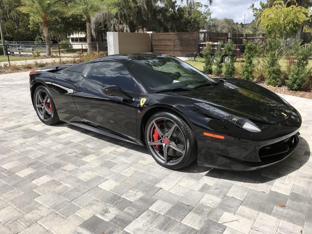 A black ferrari 458 spider is parked on a brick driveway.