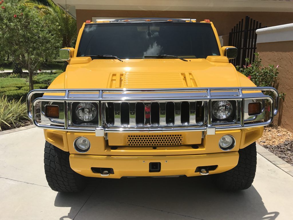 A yellow hummer is parked in a driveway in front of a house.