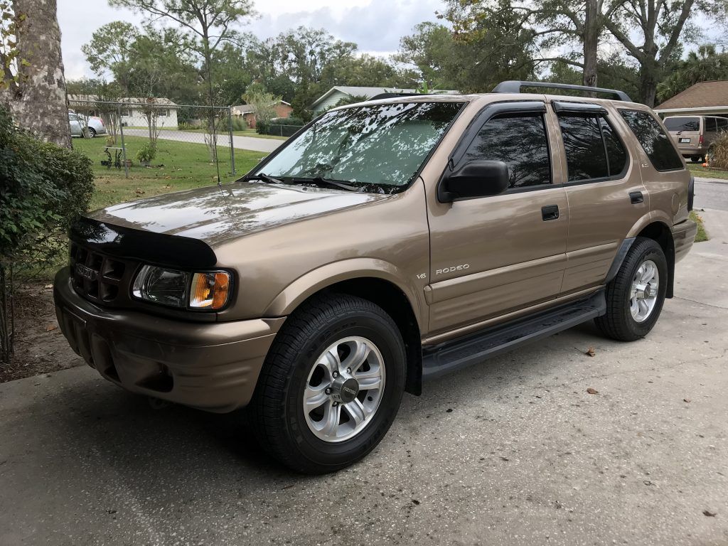 A brown suv is parked in a driveway next to trees.