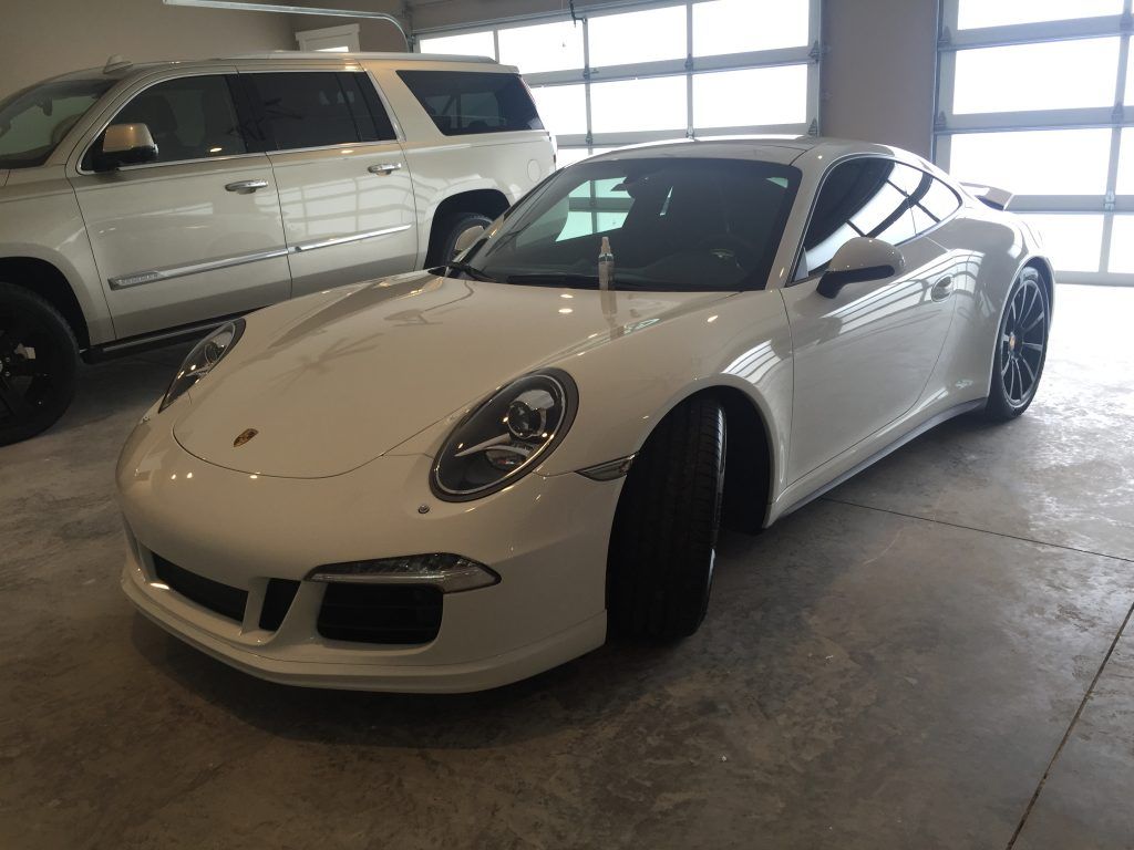 A white porsche 911 is parked in a garage next to a white suv.