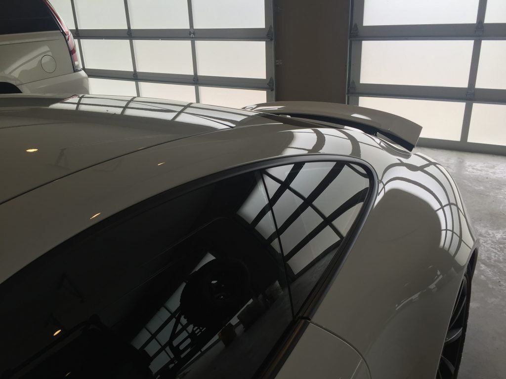 A white car with a spoiler on the roof is parked in a garage