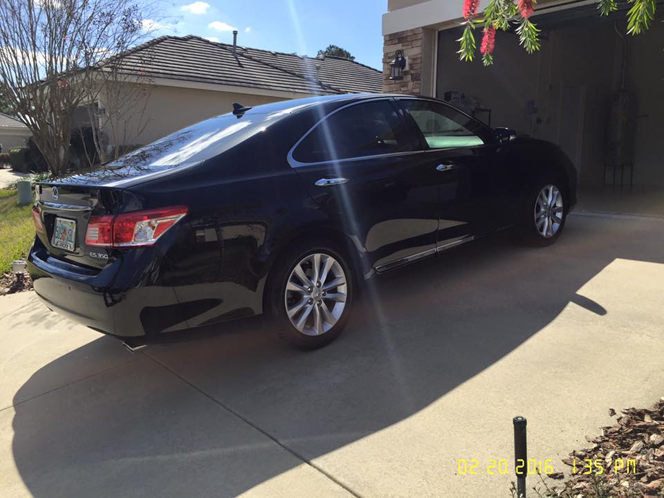 A black car is parked in a driveway in front of a house.