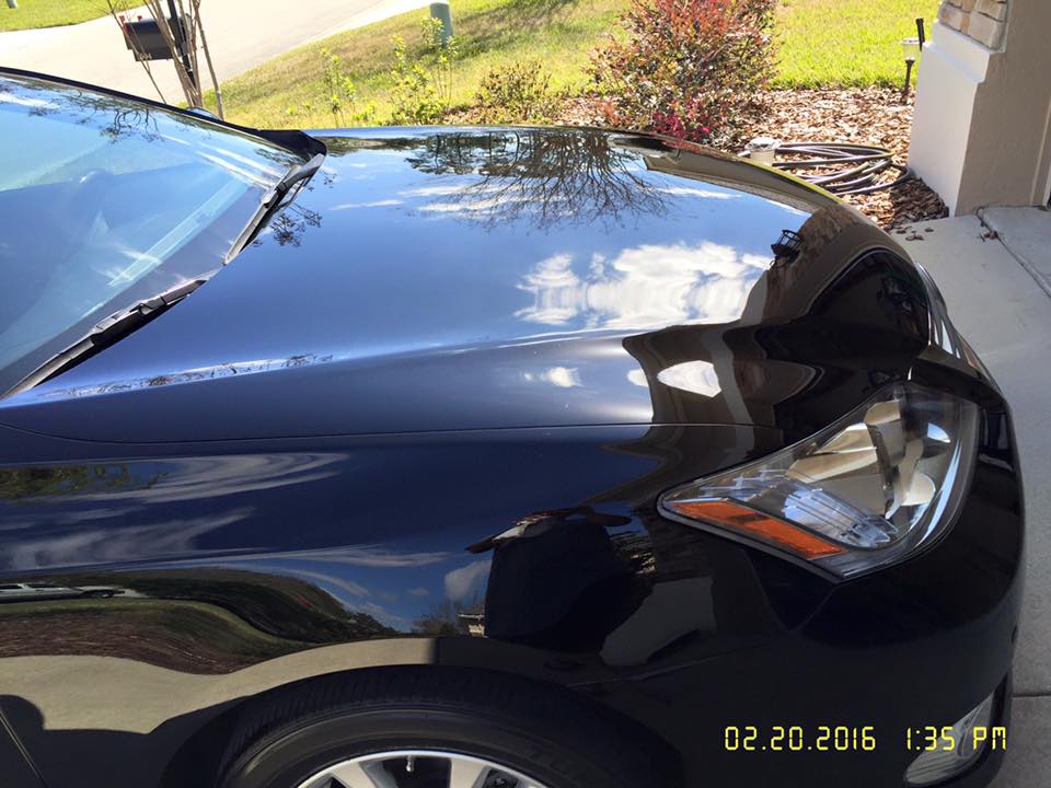 A black car is parked in a driveway on a sunny day.