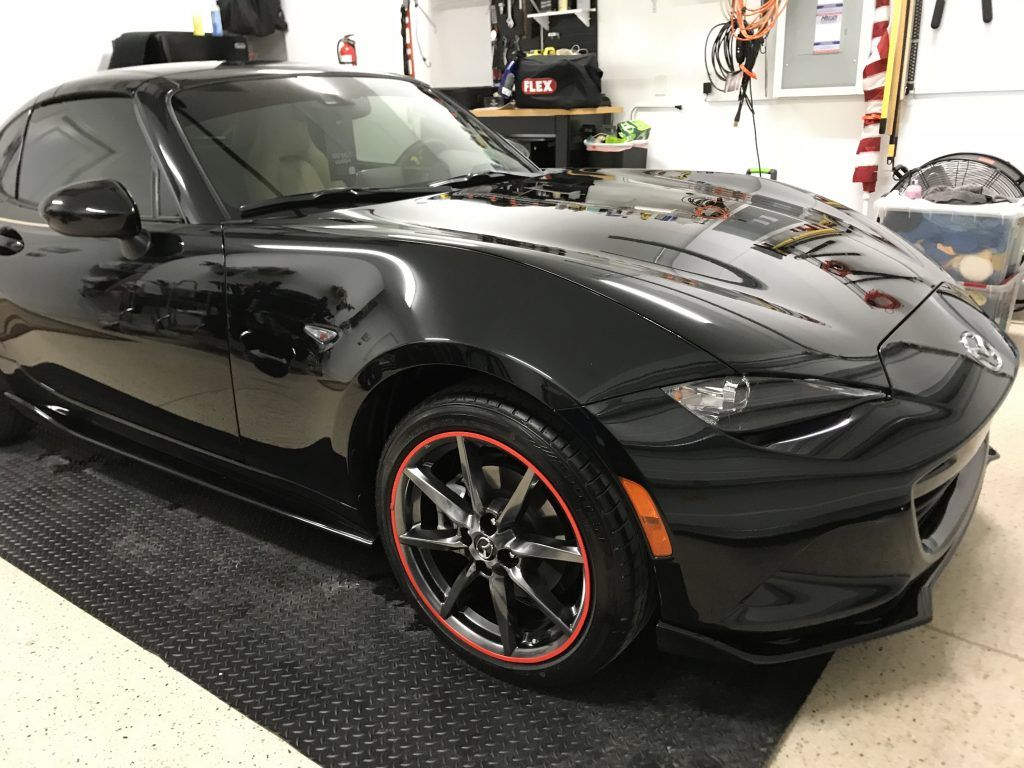 A black sports car with red rims is parked in a garage.