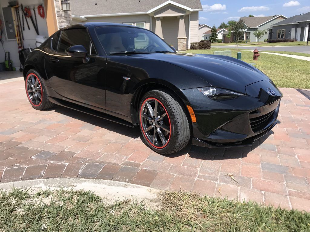 A black sports car is parked on a brick driveway in front of a house.