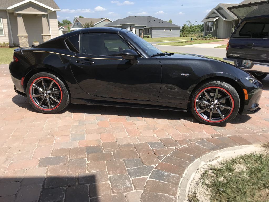 A black sports car with red wheels is parked on a brick driveway.