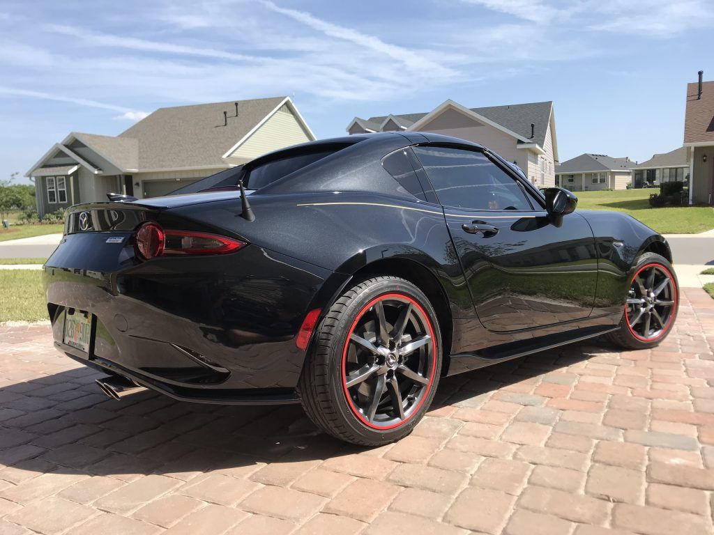 A black sports car with red wheels is parked on a brick driveway.