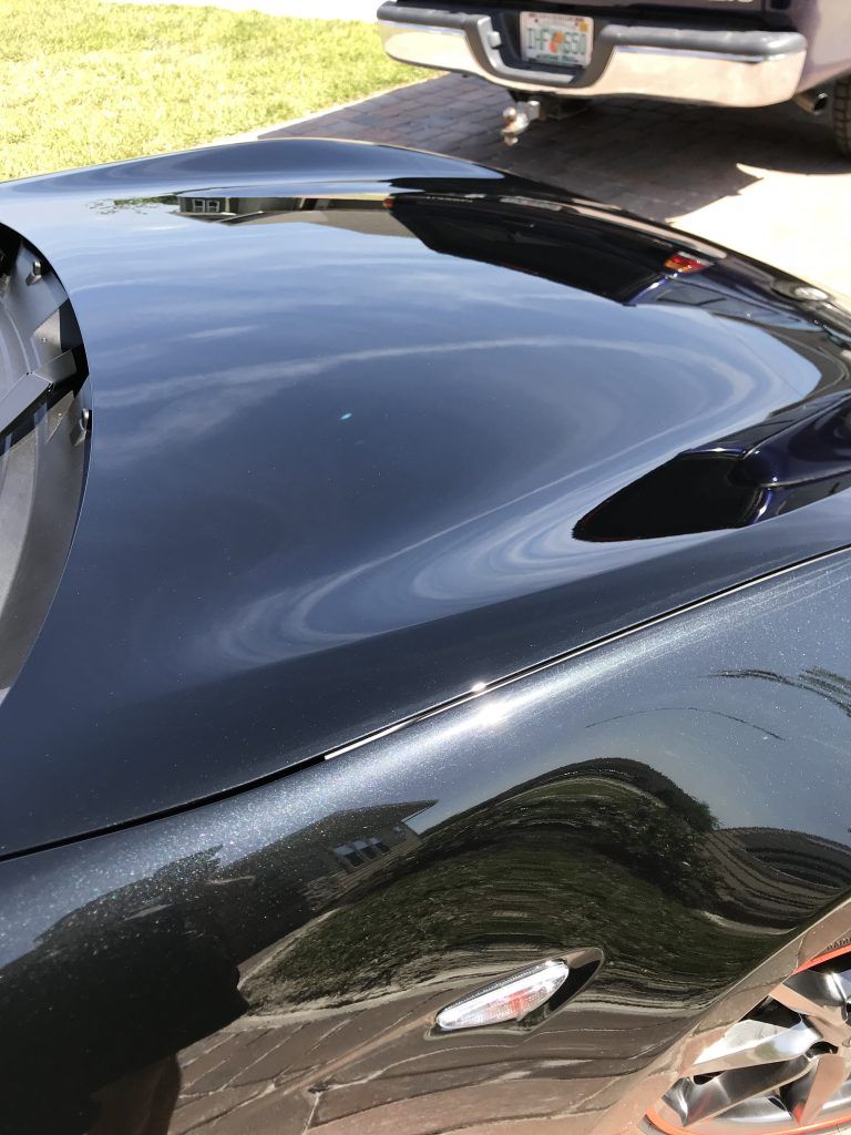 A black car is parked in a driveway next to a truck.