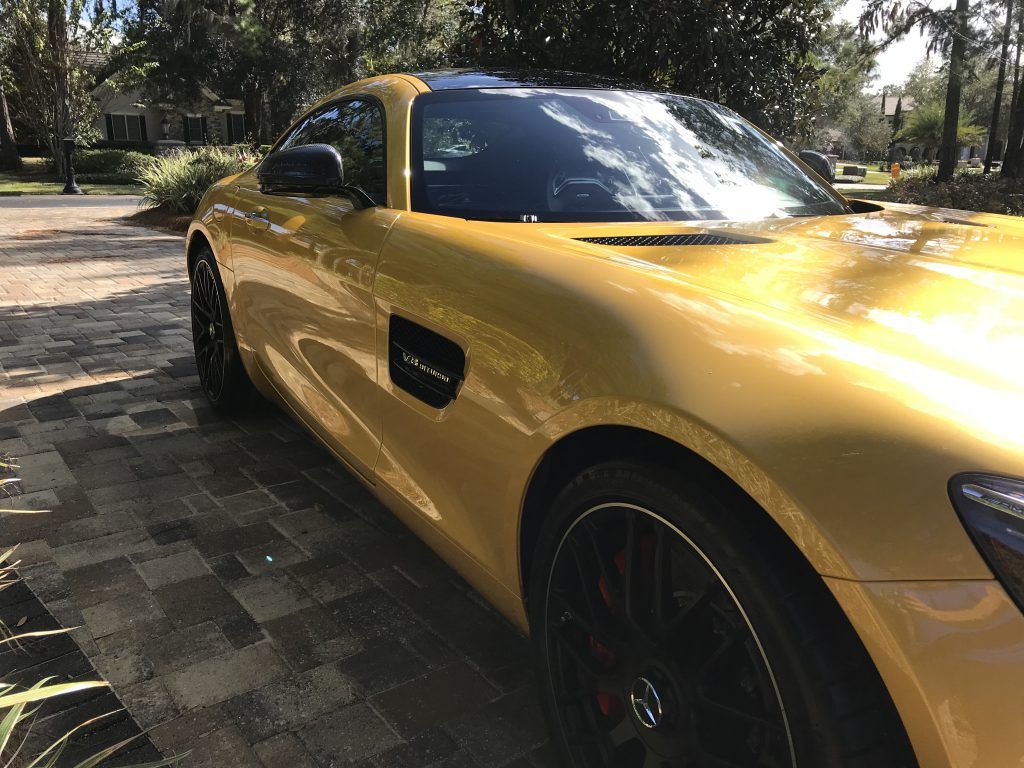 A yellow sports car is parked on a brick driveway.