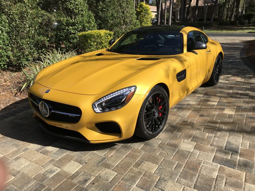 A yellow mercedes benz amg gt is parked on a brick driveway.